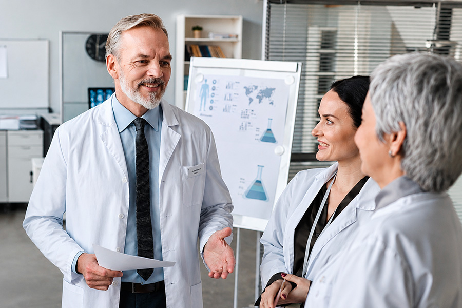 Team di medici che parla durante una riunione clinica, con grafici scientifici visibili sullo sfondo